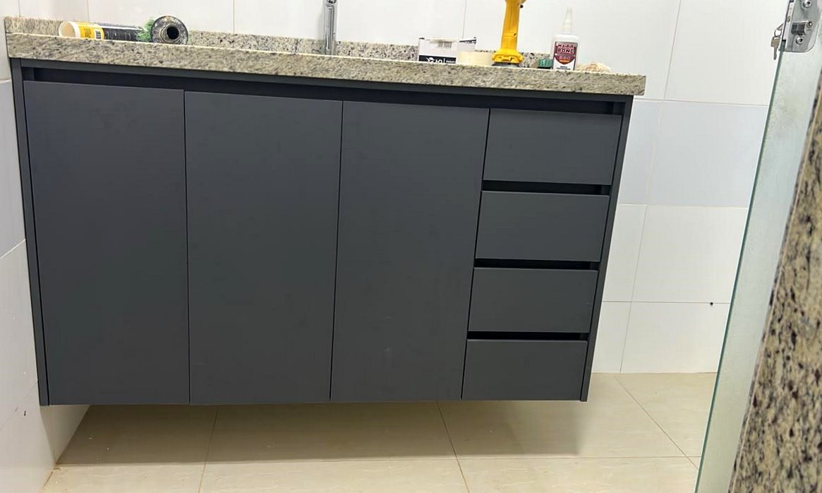 Gabinete de banheiro em grafite sob bancada de granito, com portas e gavetas